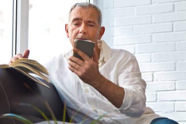 man with book and mobile phone on the sofa at home