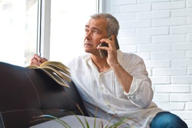 man with book and mobile phone on the sofa at home