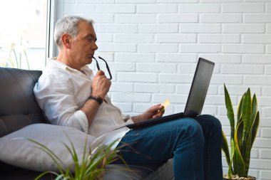 Bilgisayarı ve kredi kartı olan orta yaşlı bir adam.