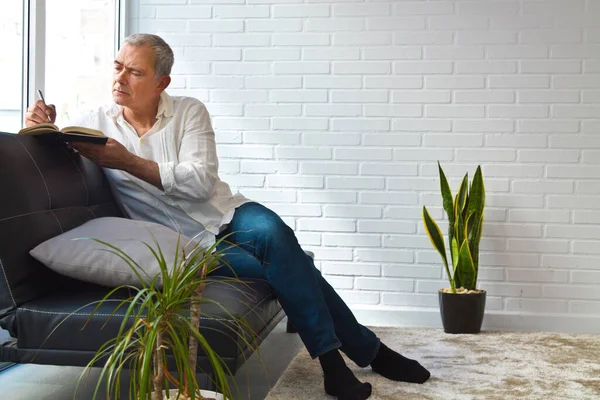 mature man writing in notebook on the sofa at home or office