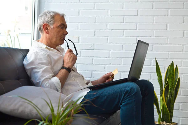 Bilgisayarı ve kredi kartı olan orta yaşlı bir adam.