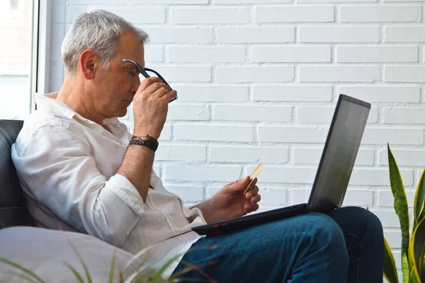 Bilgisayarı ve kredi kartı olan orta yaşlı bir adam.