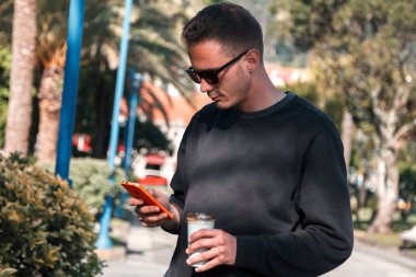 Şehirde telefonla dolaşıp kahve içen bir adam.