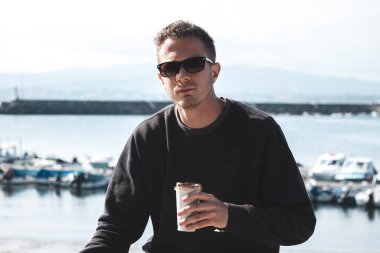 Genç adam gezinti güvertesinde oturup kahve içiyor.