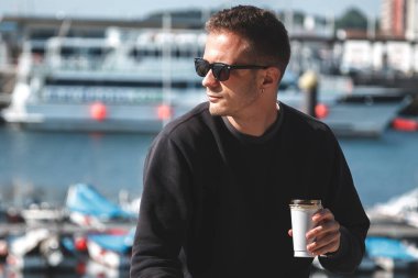 Genç adam gezinti güvertesinde oturup kahve içiyor.