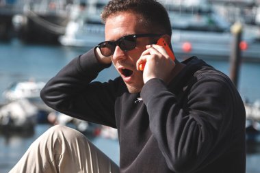 Şaşırmış suratlı bir adam deniz limanında cep telefonuyla konuşuyor. Seyahat kavramı.