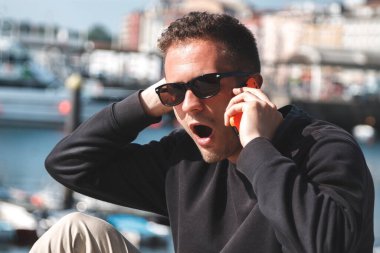 Şaşırmış suratlı bir adam deniz limanında cep telefonuyla konuşuyor. Seyahat kavramı.