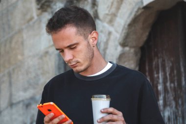 Dışarıda kahve ve cep telefonu olan bir adam var.