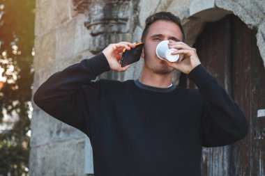 Dışarıda kahve ve cep telefonu olan bir adam var.