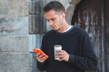 Dışarıda kahve ve cep telefonu olan bir adam var.