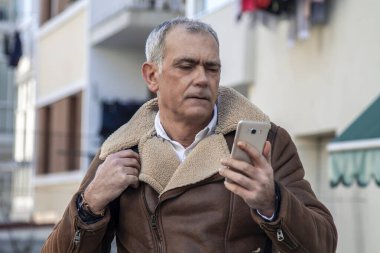 Sokakta cep telefonu kullanan olgun bir adam.