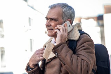 Sırt çantalı çekici, olgun bir adam sokakta telefon kullanıyor.