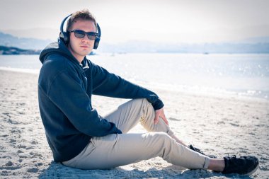 Genç adam plajda kulaklıkla dinleniyor.