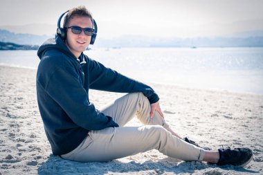 Genç adam plajda kulaklıkla dinleniyor.