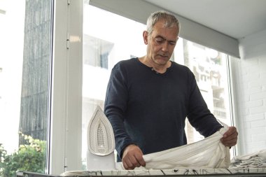 İnsan evde demirle ütü yapıyor, ev işlerinde eşitlik kavramı.