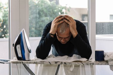 Evde ütü yapan aşırı stresli bir adam ev işlerinde demir ve konsept eşitliğiyle boğuşuyor