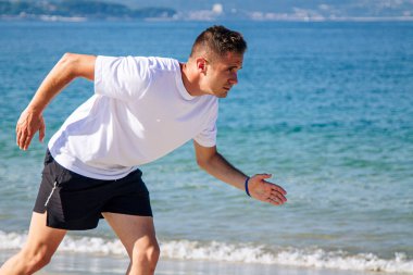 Genç adam sahilde koşmak için başlangıç pozisyonunda.