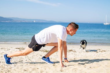 Genç adam sahilde koşmak için başlangıç pozisyonunda.