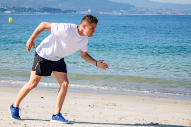 Genç adam sahilde koşmak için başlangıç pozisyonunda.