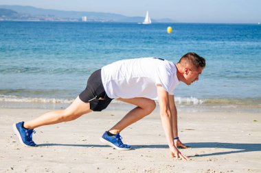 Genç adam sahilde koşmak için başlangıç pozisyonunda.