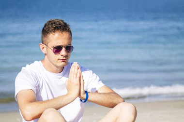 Kumsalda dinlenmek için yoga yapan bir adam.