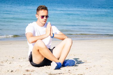 Kumsalda dinlenmek için yoga yapan bir adam.