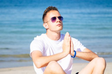 Kumsalda dinlenmek için yoga yapan bir adam.