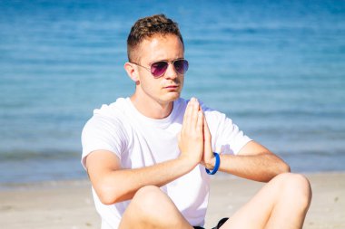 Kumsalda dinlenmek için yoga yapan bir adam.