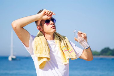 Kumsalda spordan sonra yorgun ve yorgun adam su içiyor.