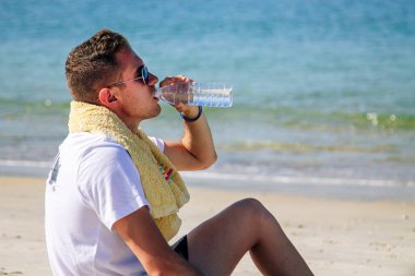 Kumsalda koşudan sonra dinlenen ve içen bir sporcu.