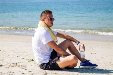 Kumsalda koşudan sonra dinlenen ve içen bir sporcu.