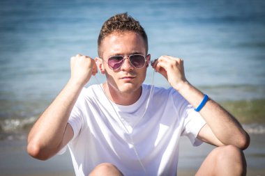 Plajda kulaklığı ve cep telefonu olan rahat bir adam.