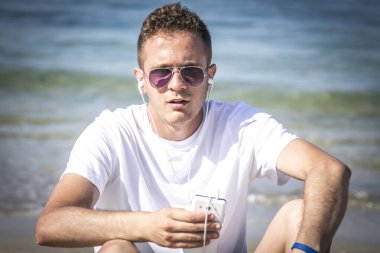 Plajda kulaklığı ve cep telefonu olan rahat bir adam.