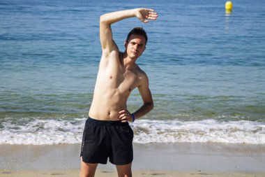 Sahilde kol ve bacak egzersizi yapan bir adam.