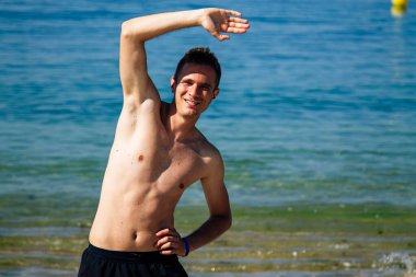 Sahilde kol ve bacak egzersizi yapan bir adam.