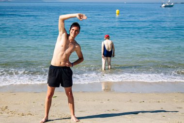 Sahilde kol ve bacak egzersizi yapan bir adam.