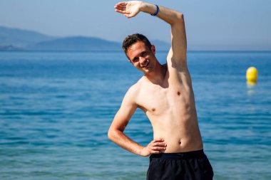 Sahilde kol ve bacak egzersizi yapan bir adam.