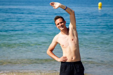 Sahilde kol ve bacak egzersizi yapan bir adam.