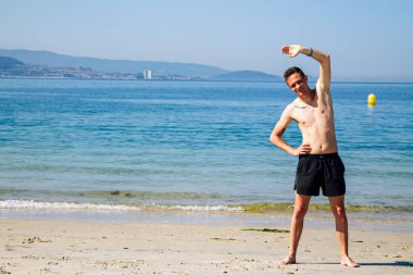 Sahilde kol ve bacak egzersizi yapan bir adam.