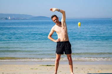 Sahilde kol ve bacak egzersizi yapan bir adam.