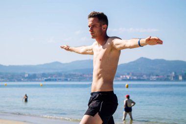 Genç adam plajda rahatlama egzersizleri yapıyor.