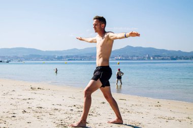 Genç adam plajda rahatlama egzersizleri yapıyor.