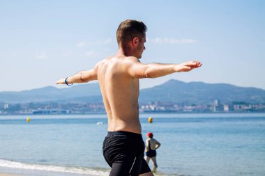 Genç adam plajda rahatlama egzersizleri yapıyor.