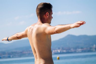 Genç adam plajda rahatlama egzersizleri yapıyor.