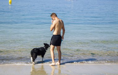 Sahilde köpekle oynayan adam.