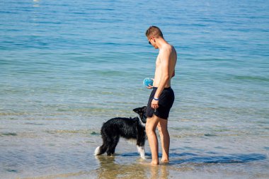 Sahilde köpekle oynayan adam.