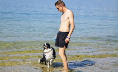 Sahilde köpekle oynayan adam.