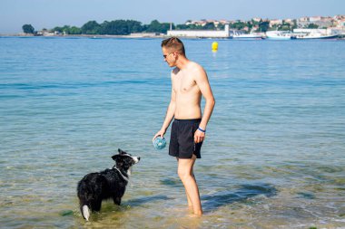 Sahilde evcil hayvanıyla oynayan bir adam.