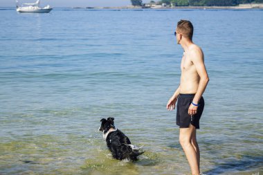 Sahilde evcil hayvanıyla oynayan bir adam.