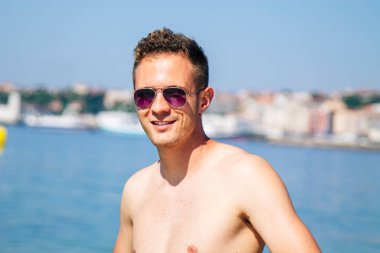 Kumsalda güneş gözlüklü yakışıklı bir genç.